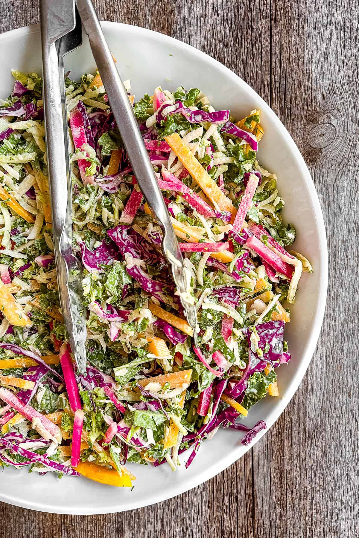 Power slaw in a shallow white salad bowl with tongs.