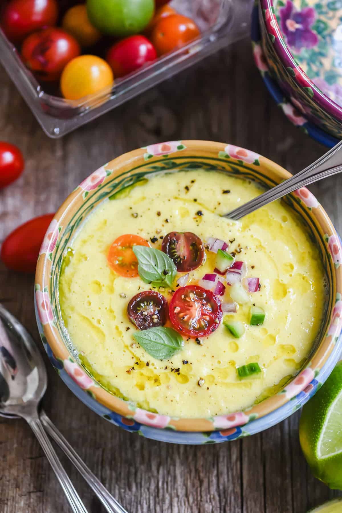 An overhead look at a small bowl of sweet corn gazpacho topped with minced veggies and cherry tomatoes.