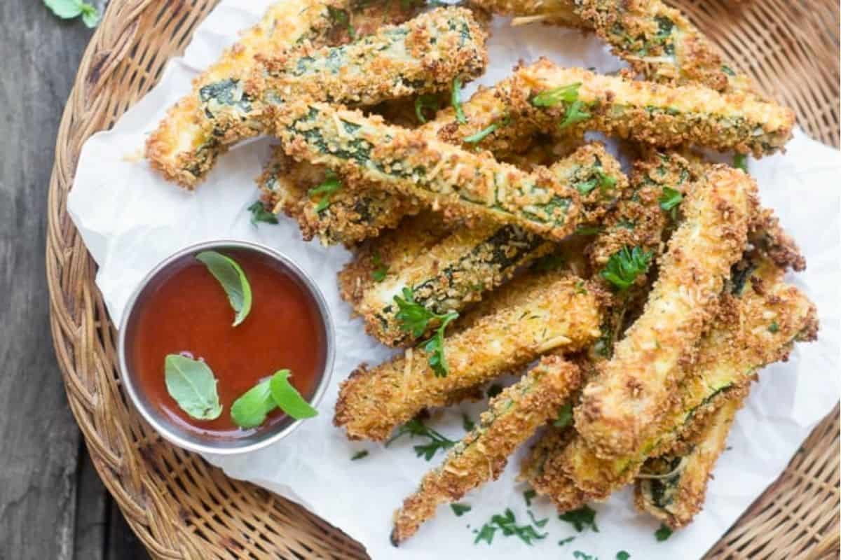 Baked Zucchini fries on a wicker plate with marinara sauce.