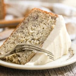 a slice of banana cake with spiced mascarpone frosting on a plate, with fork taking a bite.