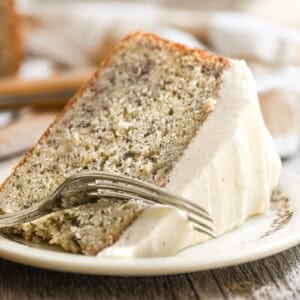 a slice of banana cake with spiced mascarpone frosting on a plate, with fork taking a bite.
