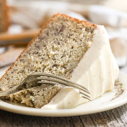 a slice of banana cake with spiced mascarpone frosting on a plate, with fork taking a bite.