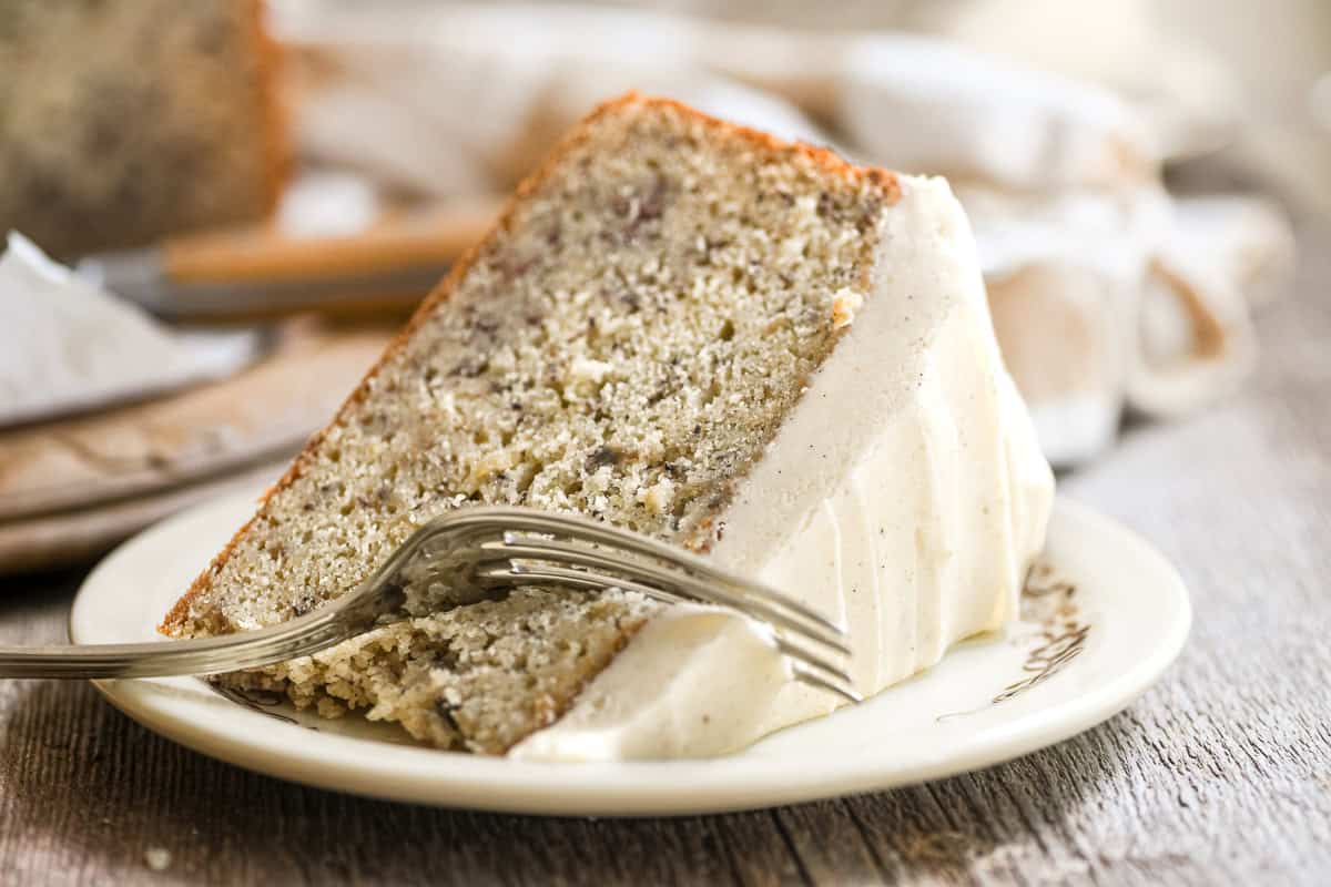 A slice of banana cake with spiced mascarpone frosting on a plate, with a fork taking a bite.