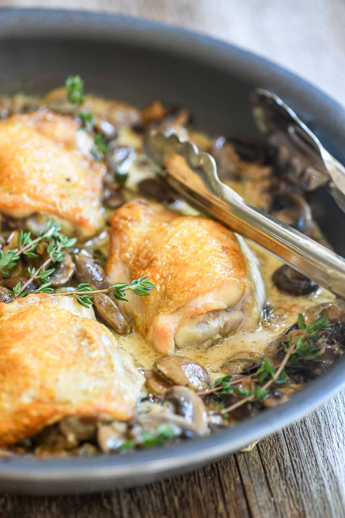 A pan of chicken thighs Marsala, just out of the oven, with tongs.