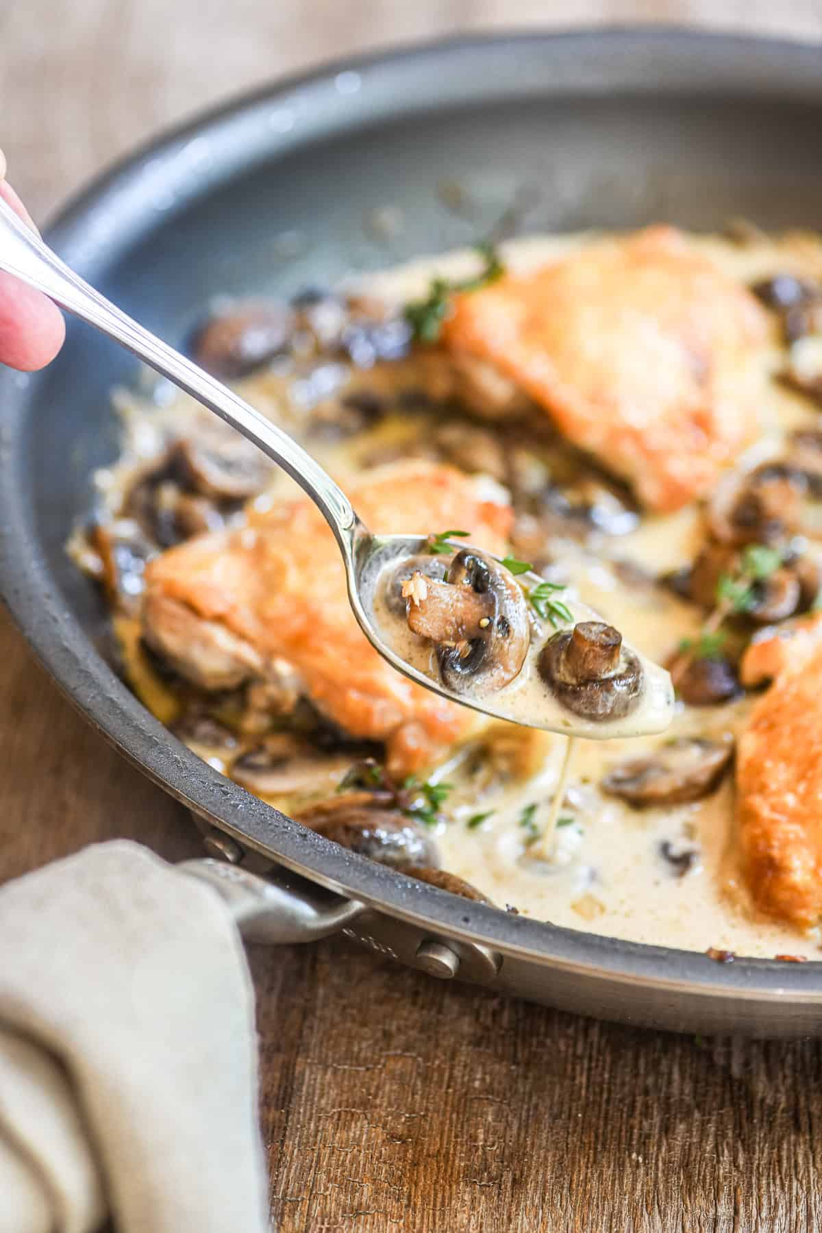 Taking a spoon of the sauce in a pan of chicken thighs Marsala.