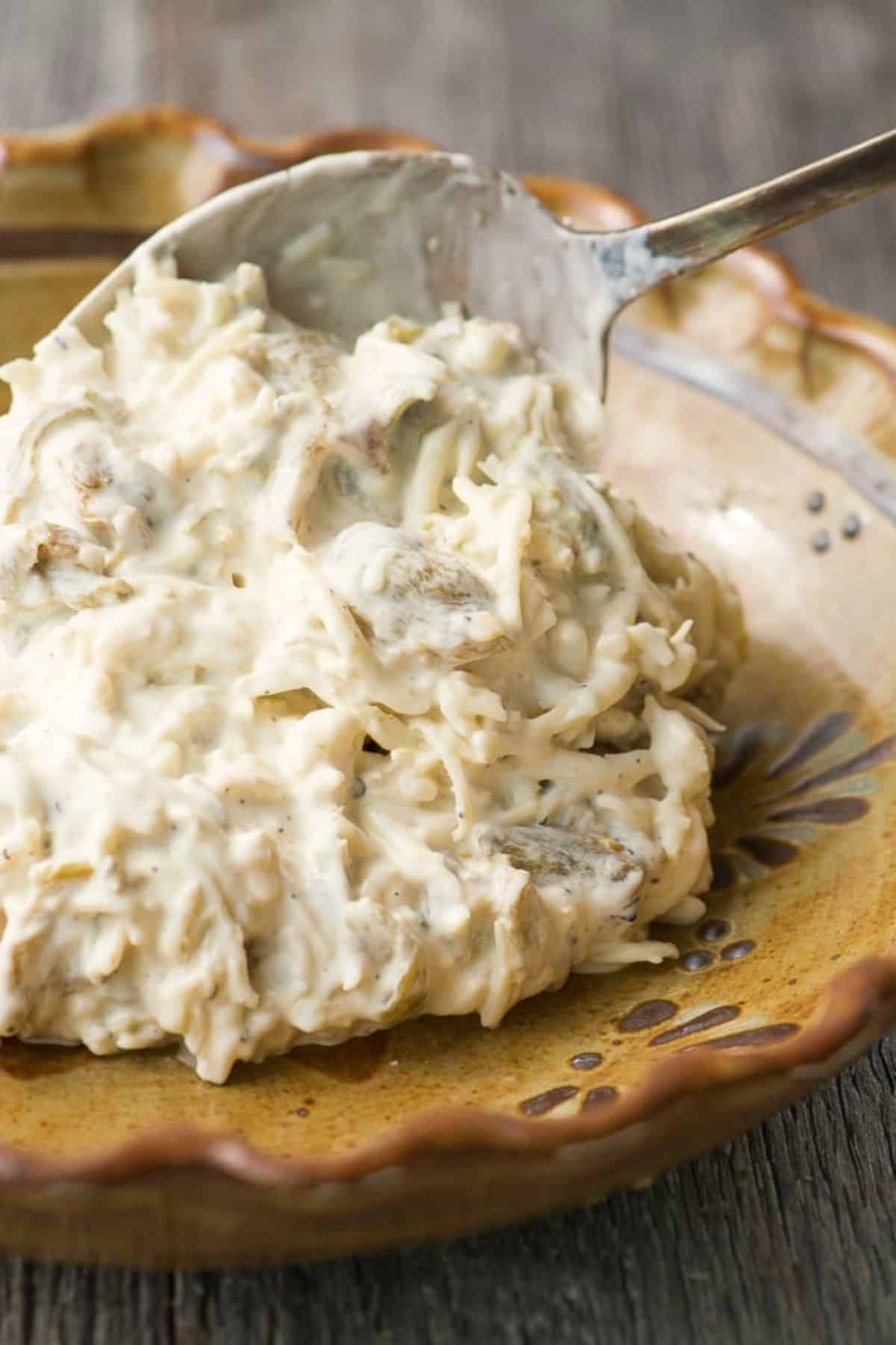 Spooning Hatch green chile dip into a baking dish.