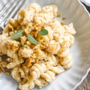 Italian pasta with walnut sauce in a shallow bowl, with sage leaves, and white wine.