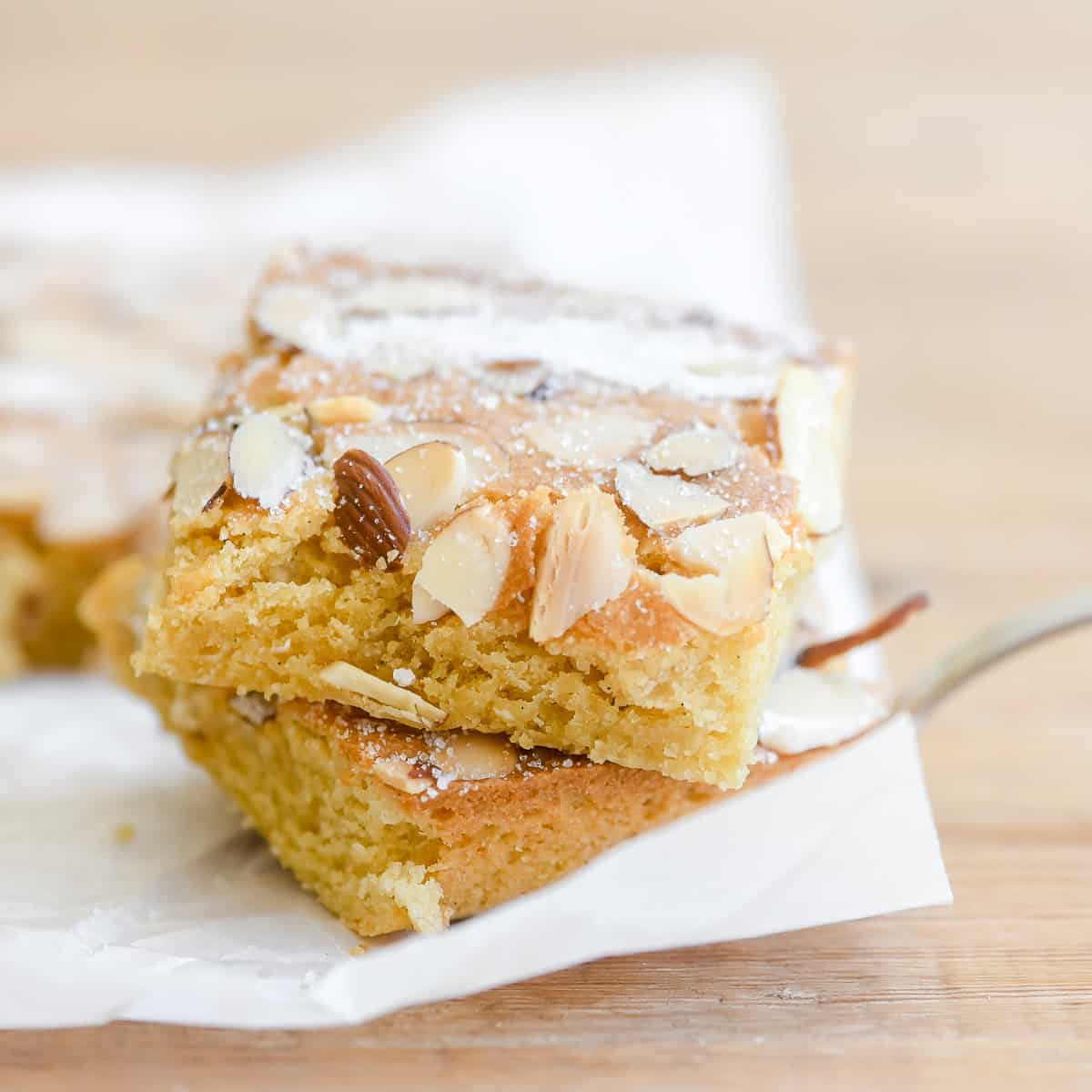 A stack of almond brownies on a fork, topped with toasted sliced almonds and sugar.
