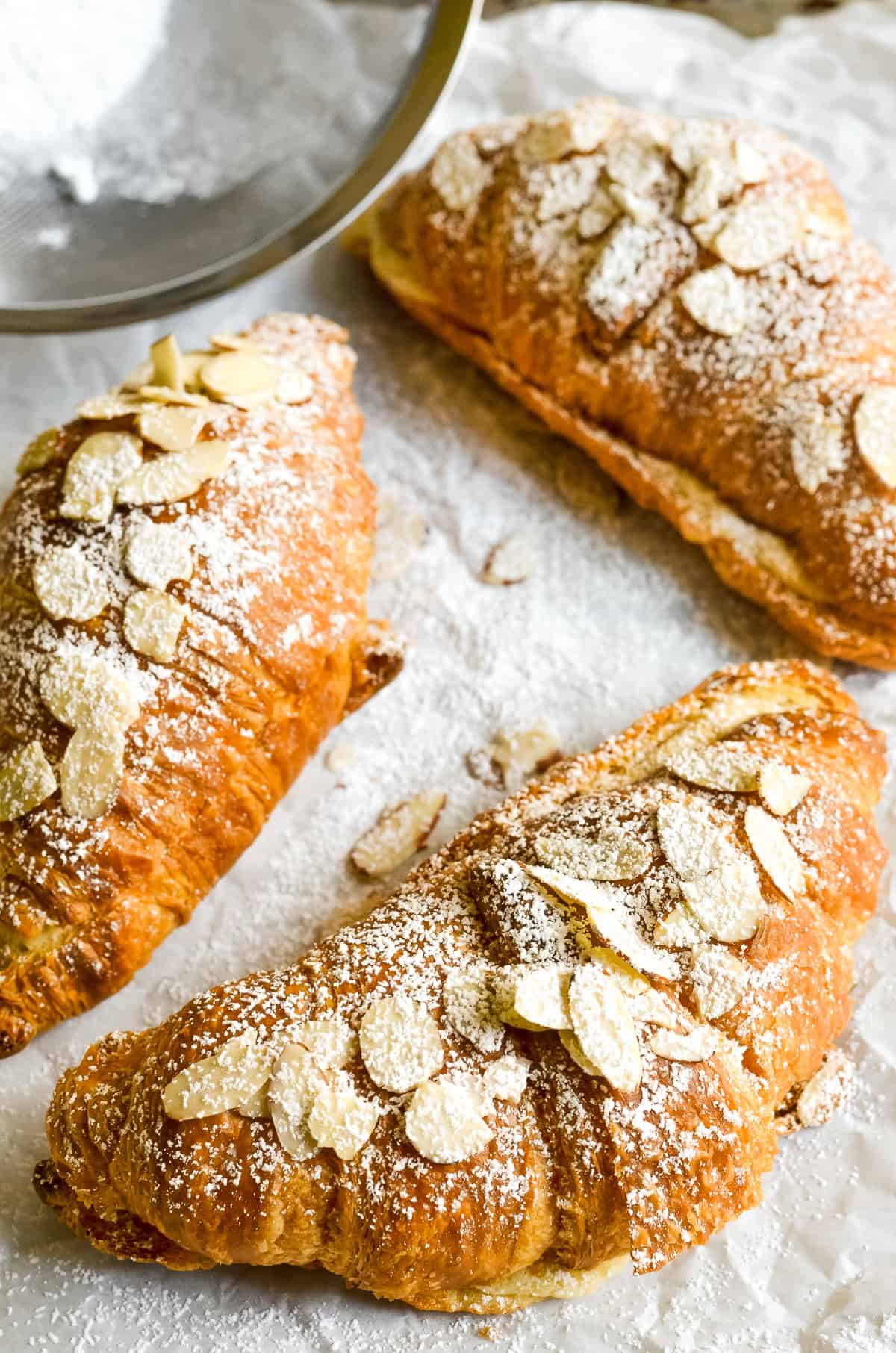 classic almond croissants, on parchment paper with powdered sugar.