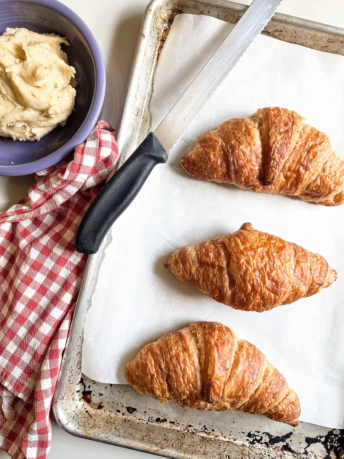 Croissants on a baking sheet with serrated knife.