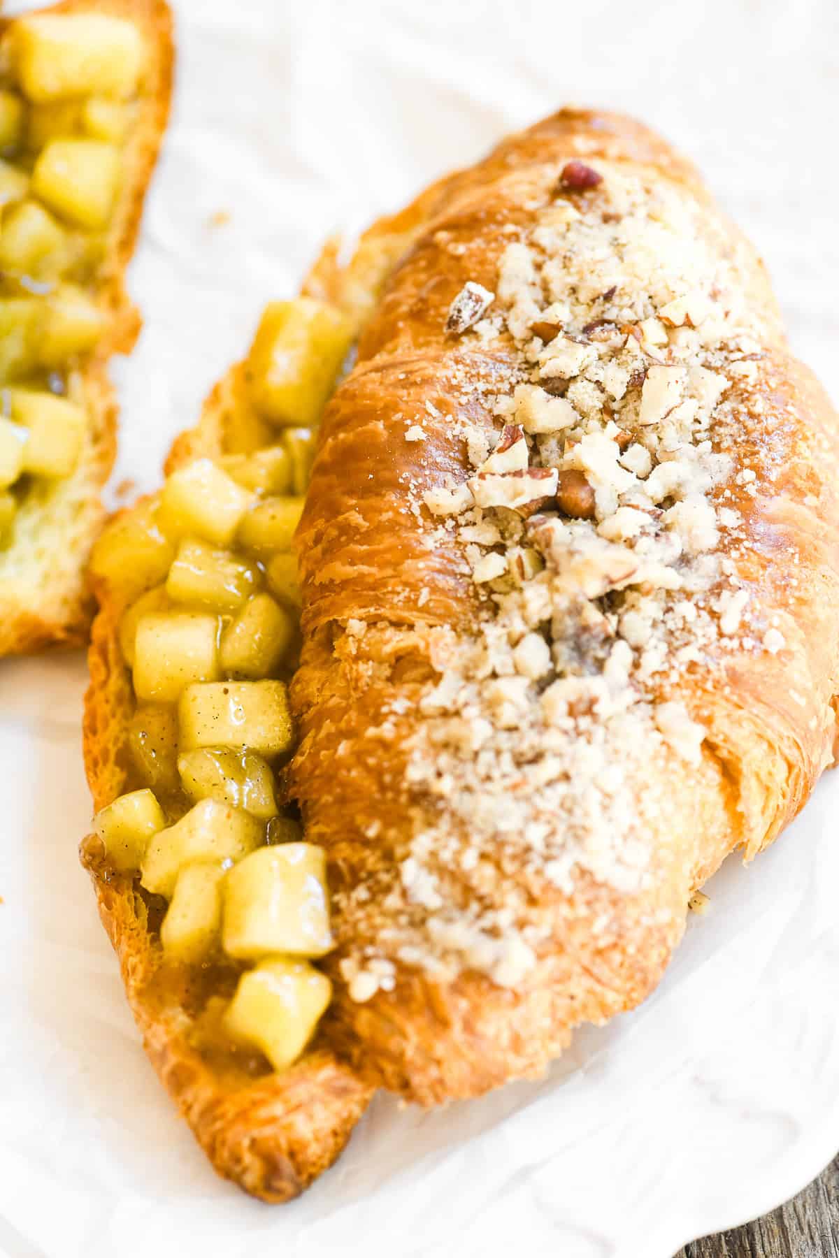 An apple pie twice baked croissant topped with pecan streusel, on crumpled parchment paper.