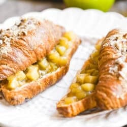 Two apple pie twice baked croissants, on a white plate.