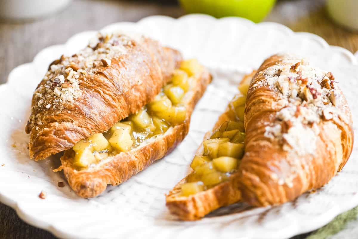 Two apple pie twice baked croissants, on a white plate.