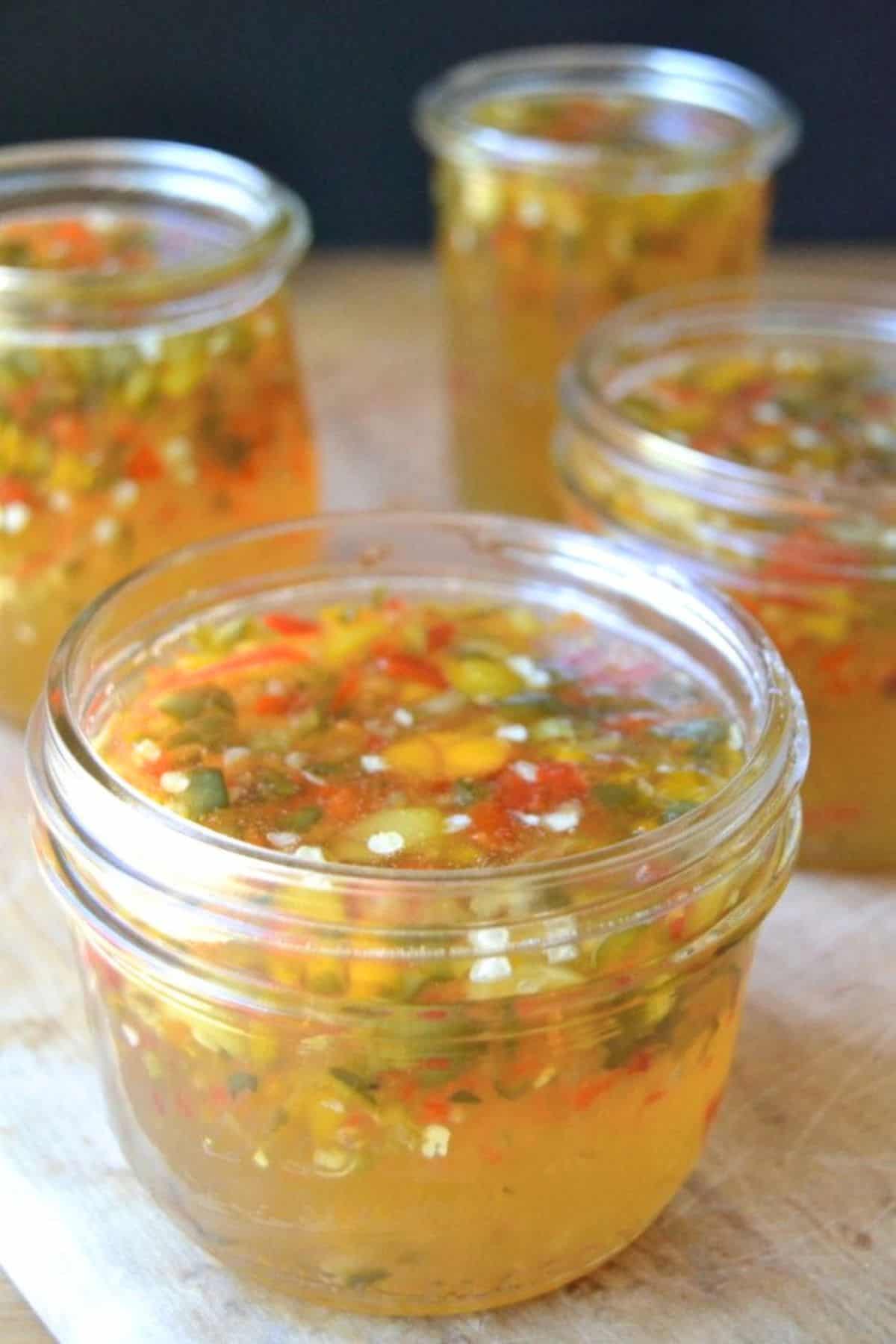Super Easy Hot Pepper Jelly is a must in every cook's arsenal. This easy recipe makes use of both sweet and hot peppers for a colorful, confetti-like look and and an intense spicy kick. #jelly #jam #hotpeppers #cheeseplate #recipe #jalapenorecipe #jalapeno #appetizer #cheeseandcrackers #FOODGIFT #THANKSGIVINGAPPETIZER #HOLIDAYAPPETIZER Golden hot pepper jelly in small glass jars.