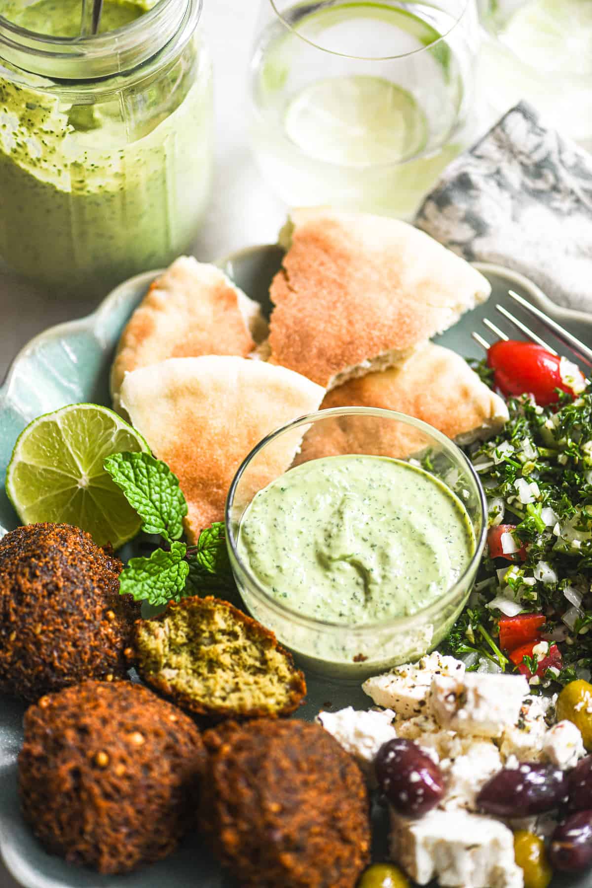 A plate of Middle Eastern style food with a small bowl of green tahini sauce in the center.