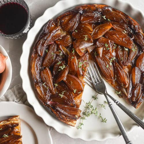Caramelized shallot tarte tatin in a white pan with slice removed.