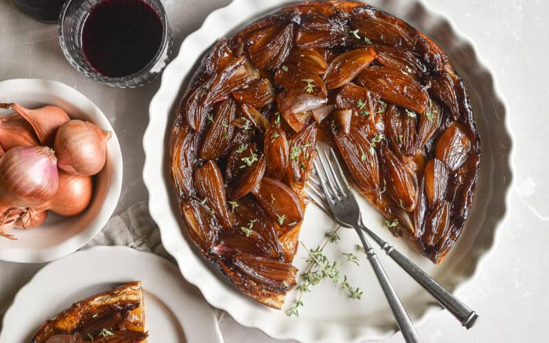 Caramelized shallot tarte tatin in a white pan with slice removed.