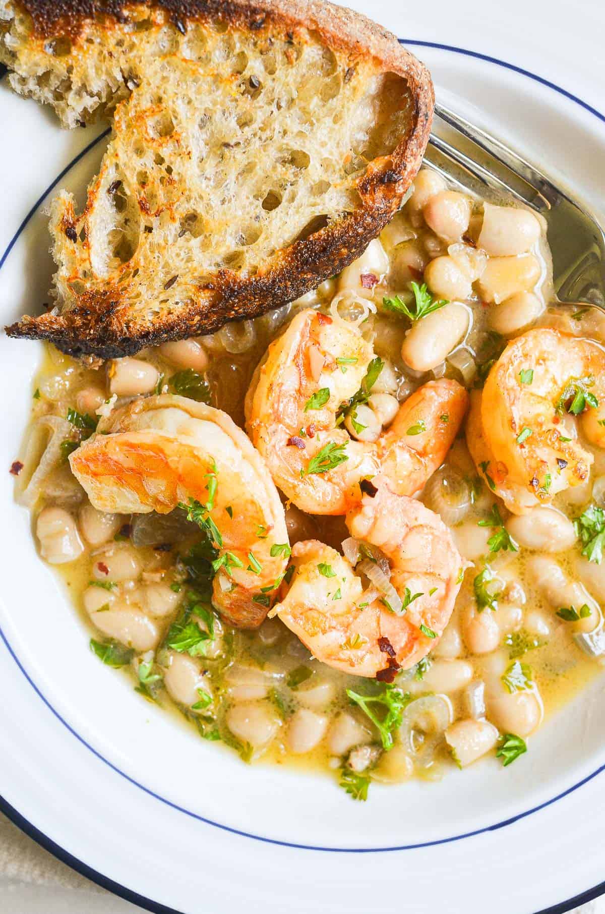 a plate of lemony shrimp and beans with a slice of toasted baguette.