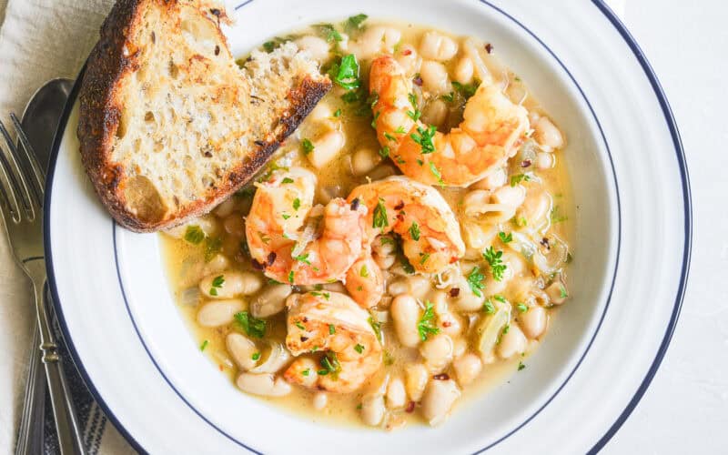 Lemony shrimp and white beans in a bowl with crusty bread.
