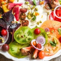 A tomato and beet salad with soft goat cheese, pistachios, and a fresh mint vinaigrette on a white platter.