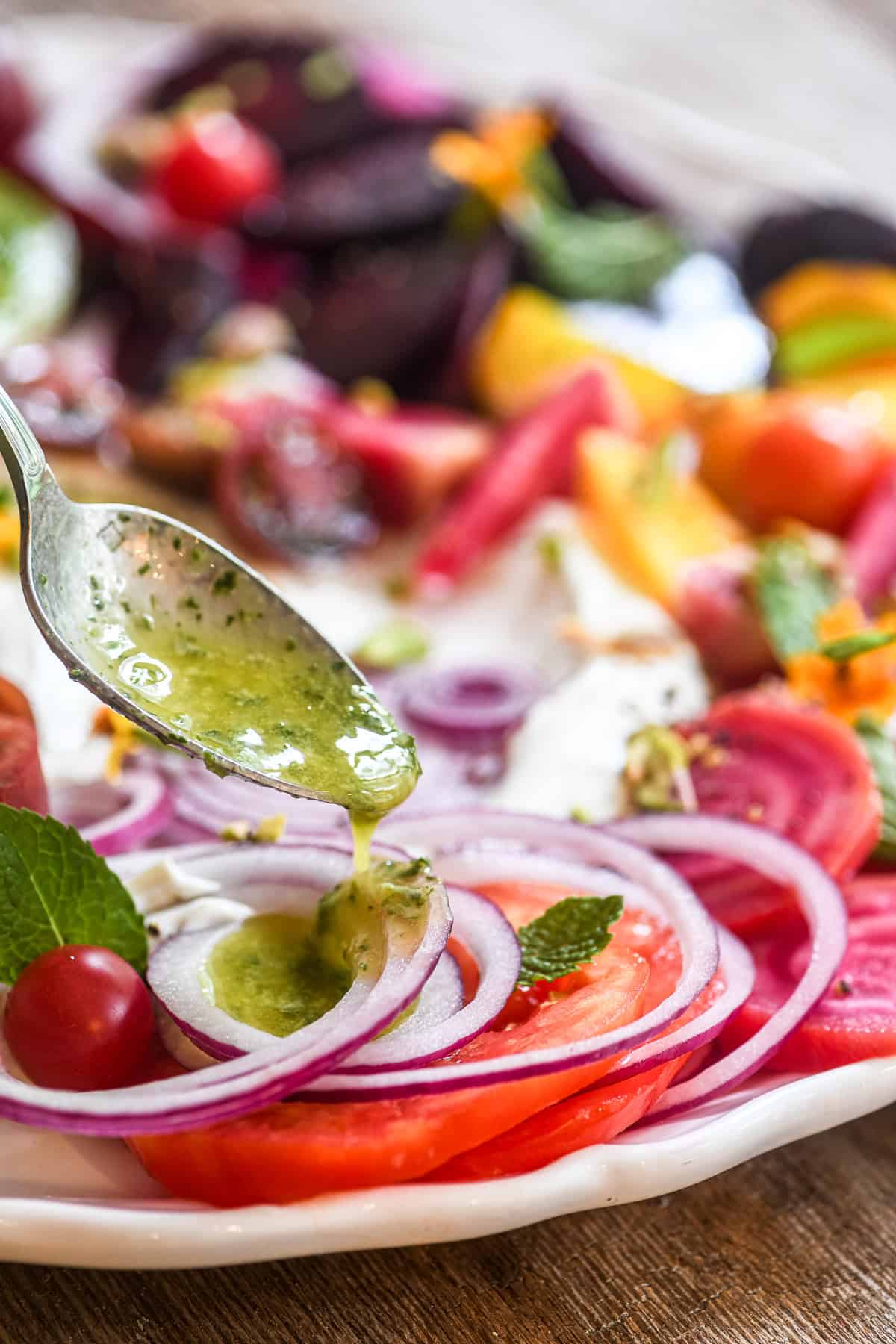 Spooning fresh mint vinaigrette on a tomato and beet salad with whipped goat cheese.