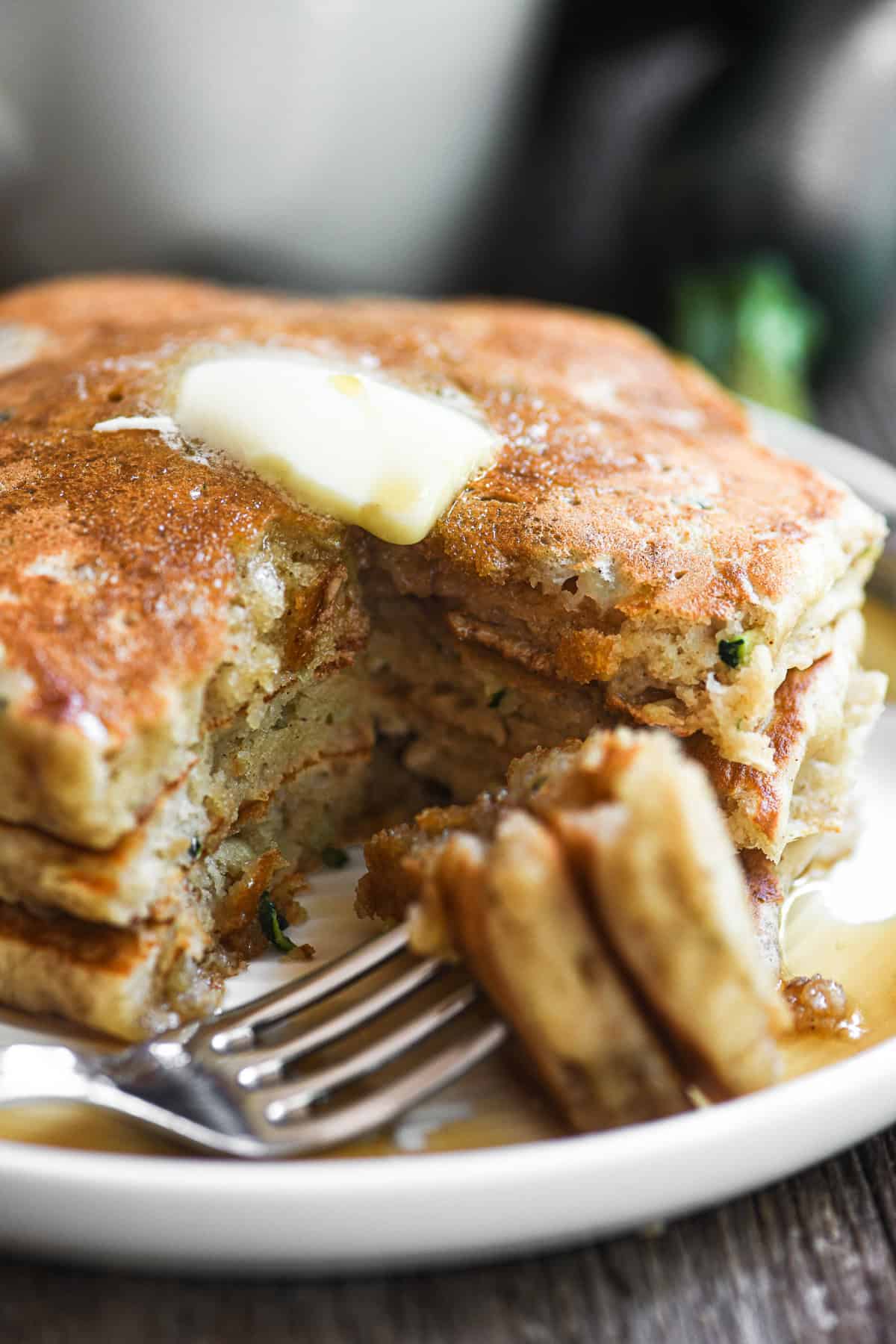 A stack of three zucchini bread pancakes topped with butter and syrup.