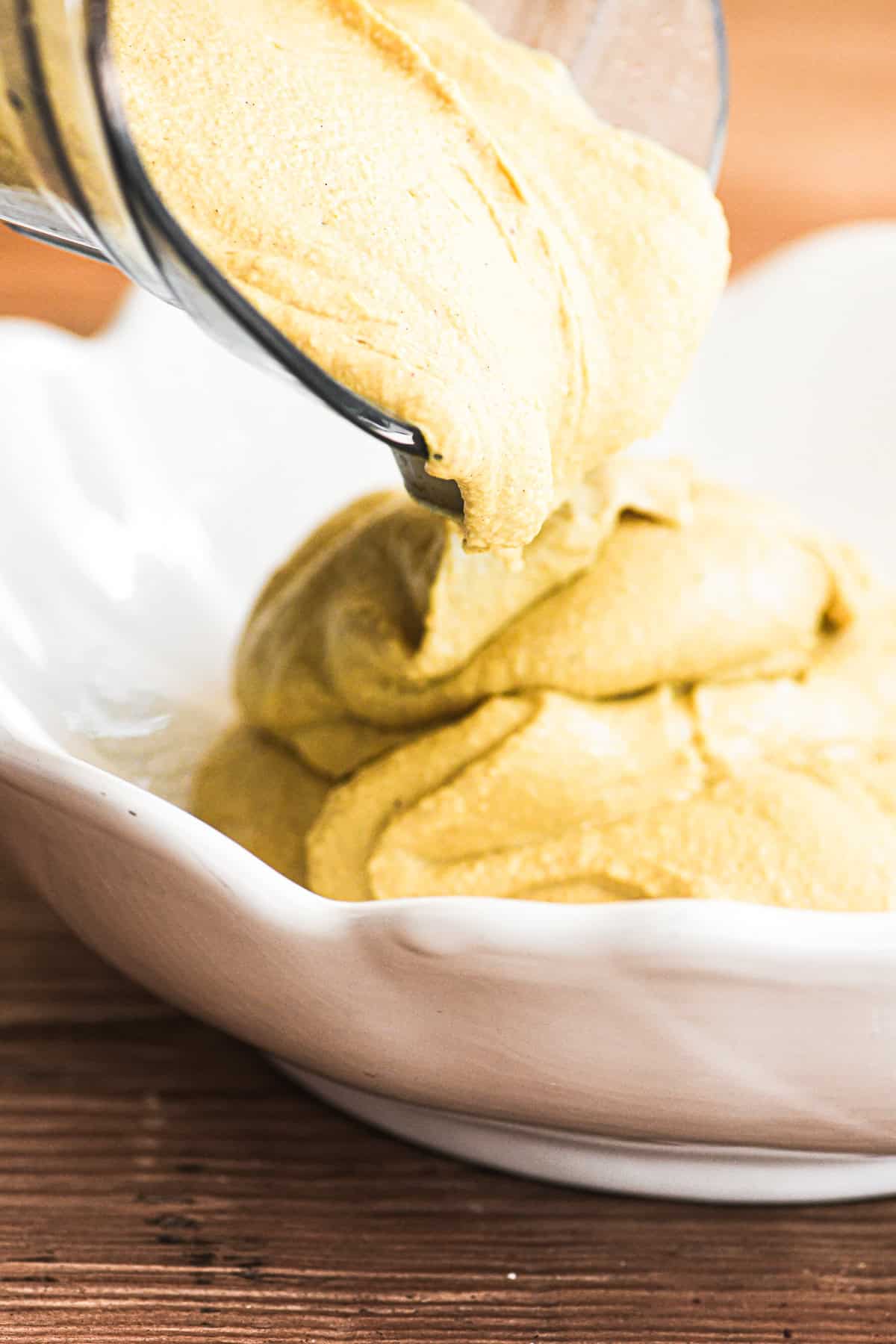 Pouring Moroccan hummus out of a blender into a bowl.