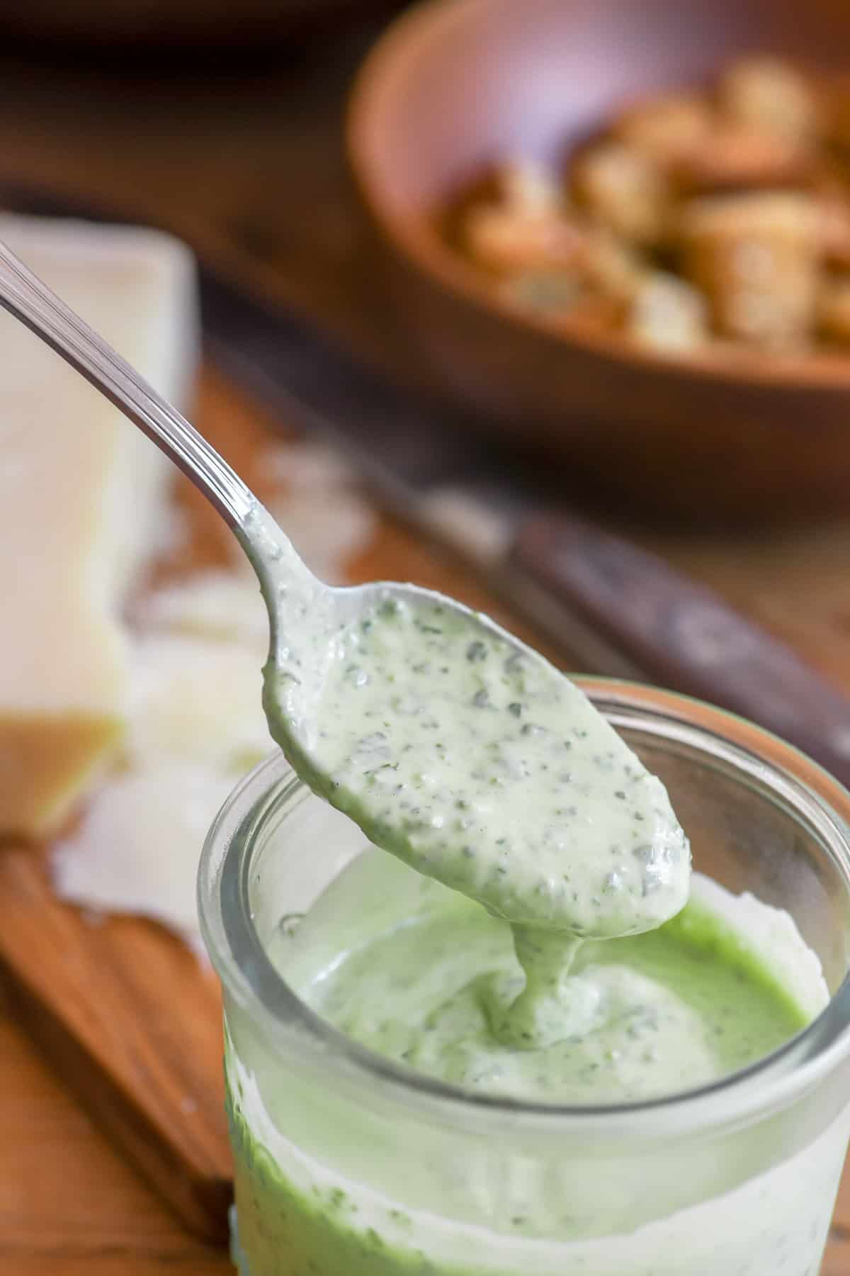 spooning pesto Caesar salad dressing out of a jar.