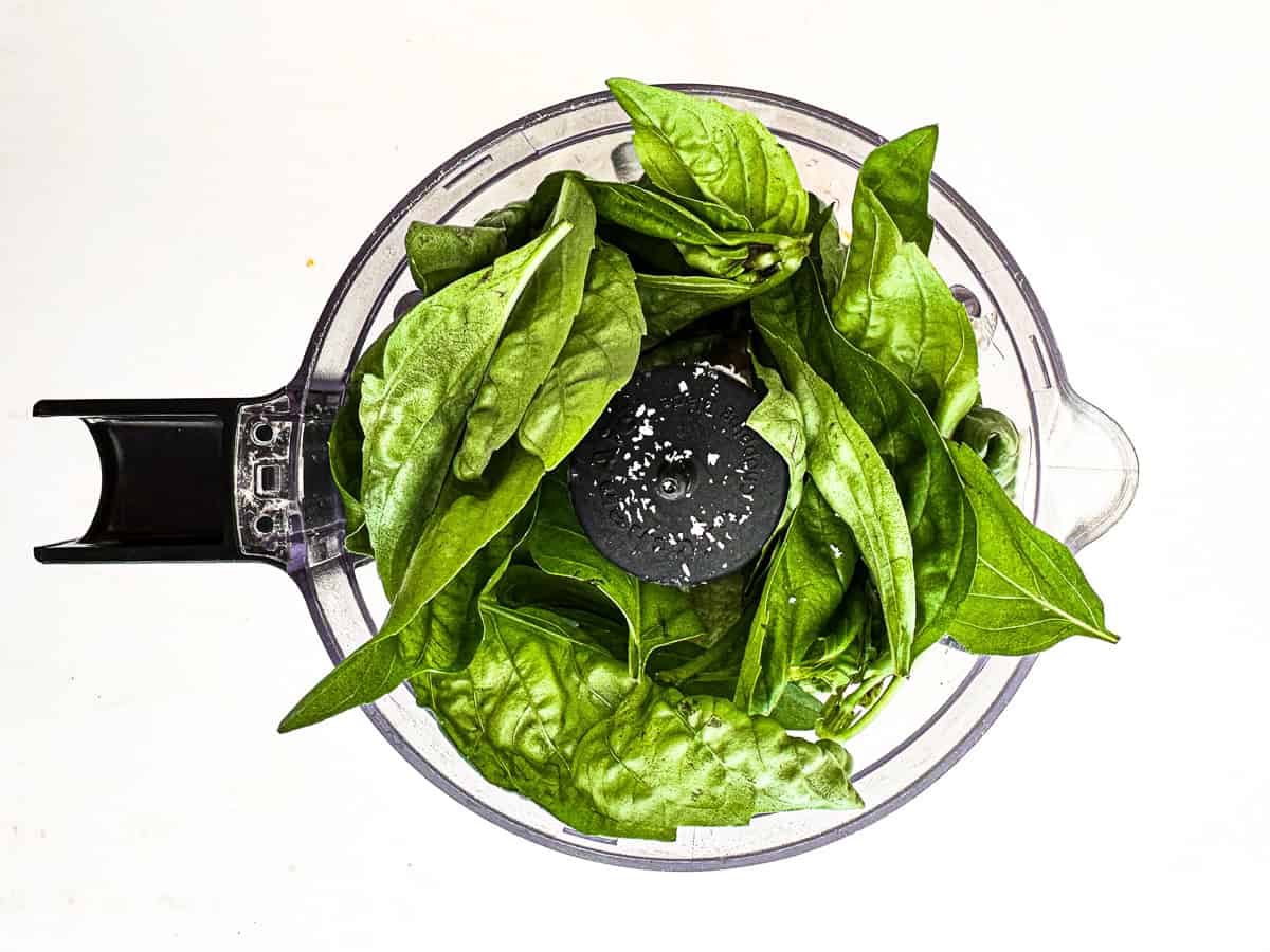 small food processor loaded with basil and other ingredients for pesto Caesar salad dressing.