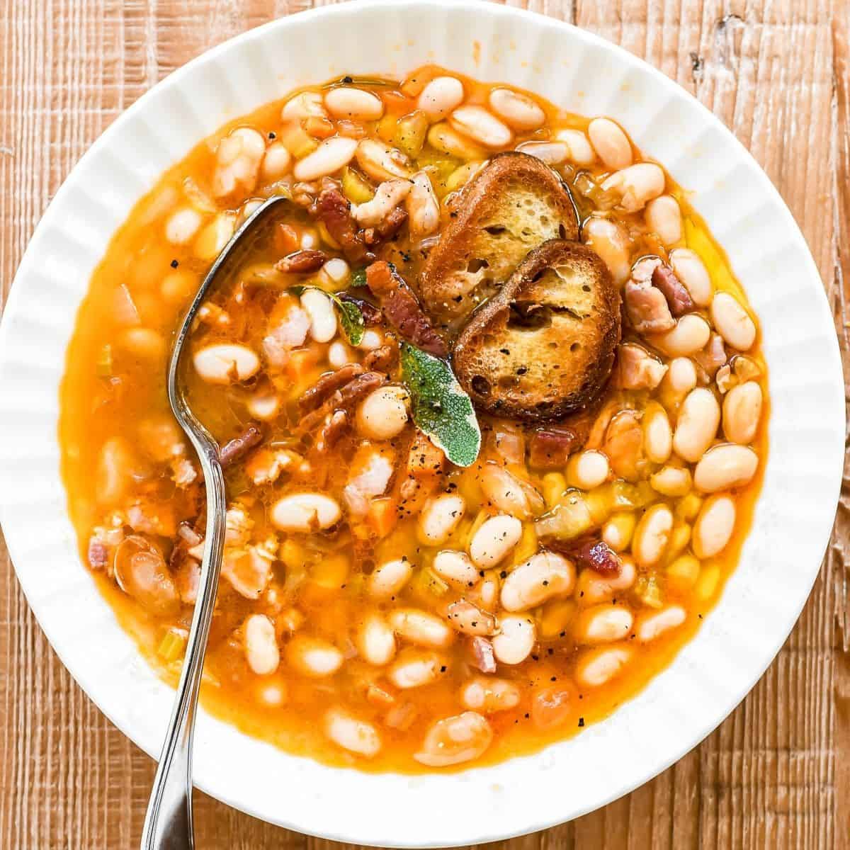 Fiber rich Tuscan bean and bacon soup in a bowl with spoon.
