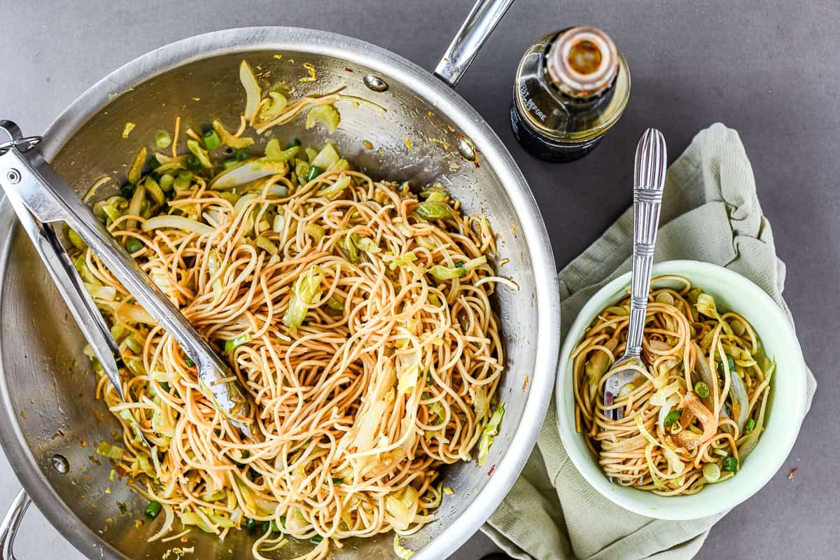 chow mein in a wok, with bowl and fork.