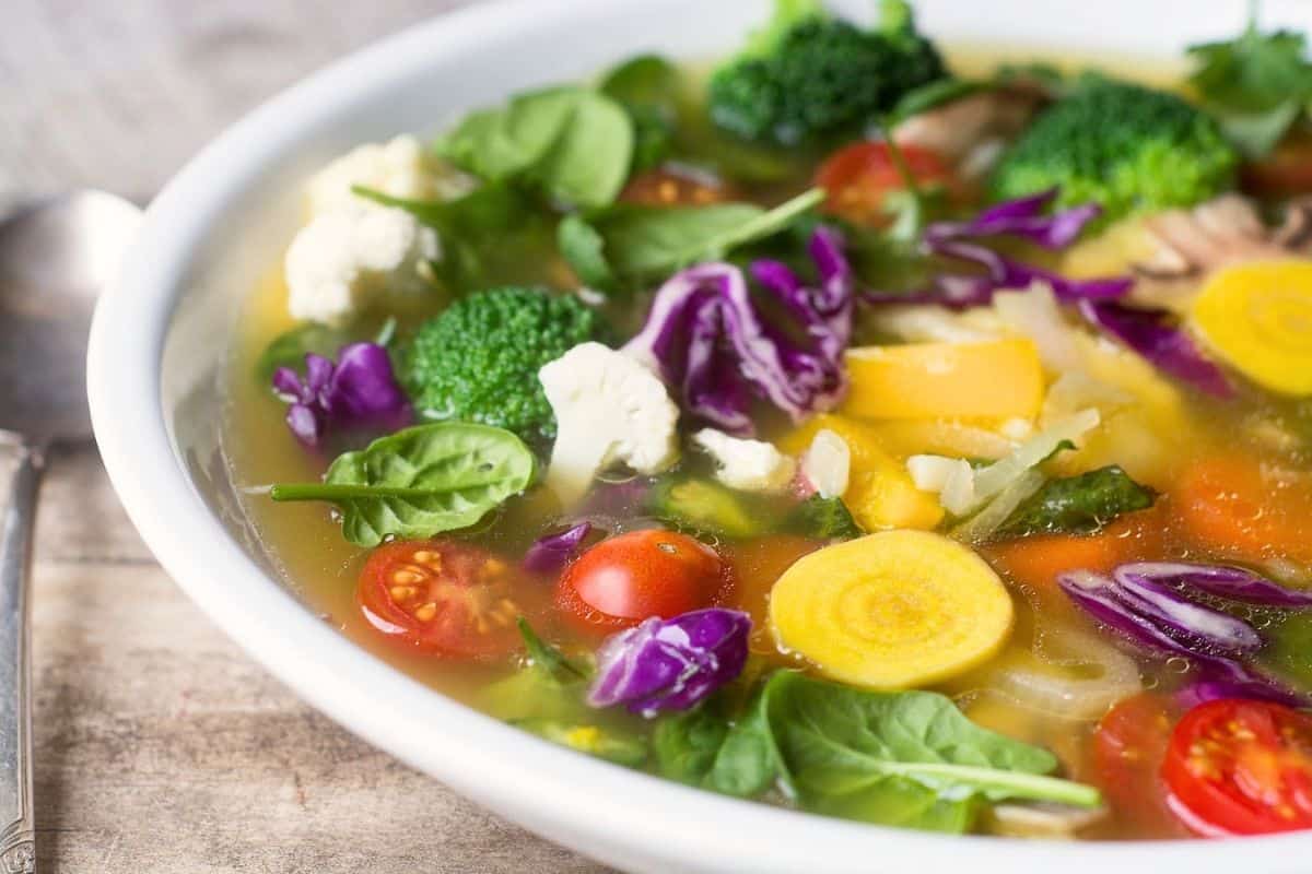 Detox vegetable soup in a white bowl with spoon.