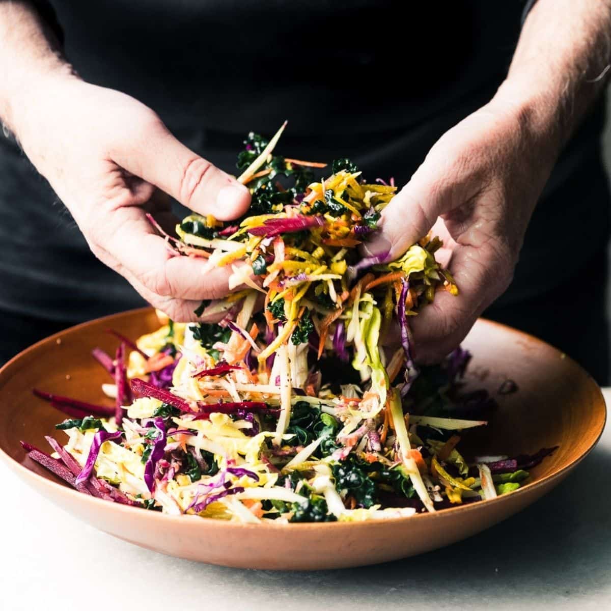 Hands tossing a vibrant Winter Slaw in a wooden bowl.